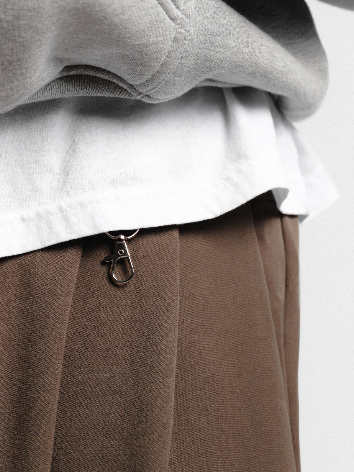 Brown pleated pants from Sweats EU featuring a tailored fit and classic design, displayed on a hanger against a neutral background.